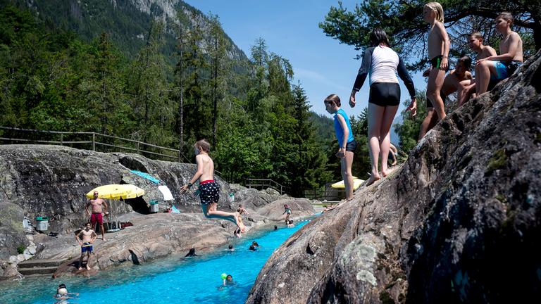 Besucher des alpinen Naturschwimmbads springen ist das Wasser am 25.06.2019 in Les Marecottes (Schweiz)