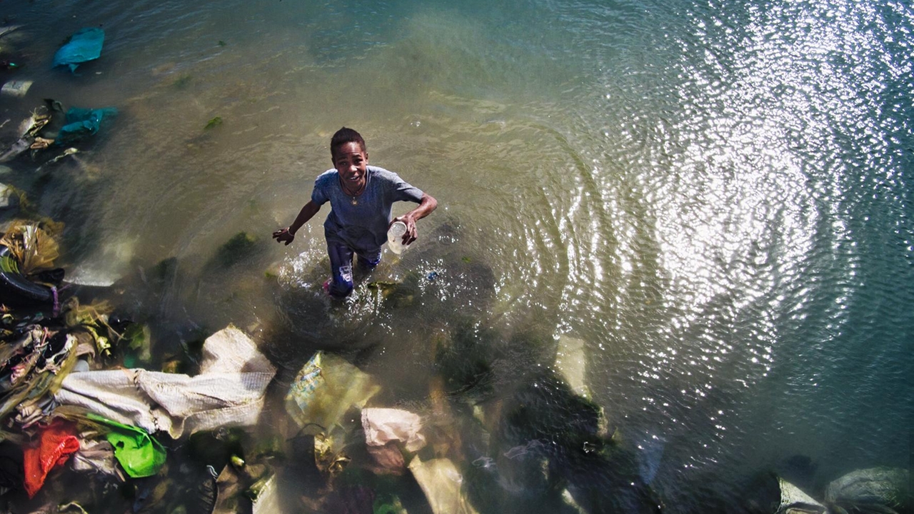 Ein Junge steht im Wasser voller Platikmüll