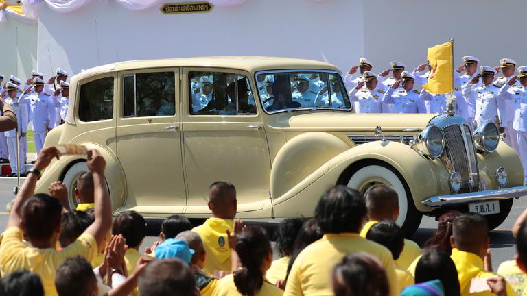 König Maha Vajiralongkorn und Königin Suthida fahren in einer Limousine während der Krönungsfeierlichkeiten am 4. Mai 2019 in Bangkok an wartenden Menschen vorbei.