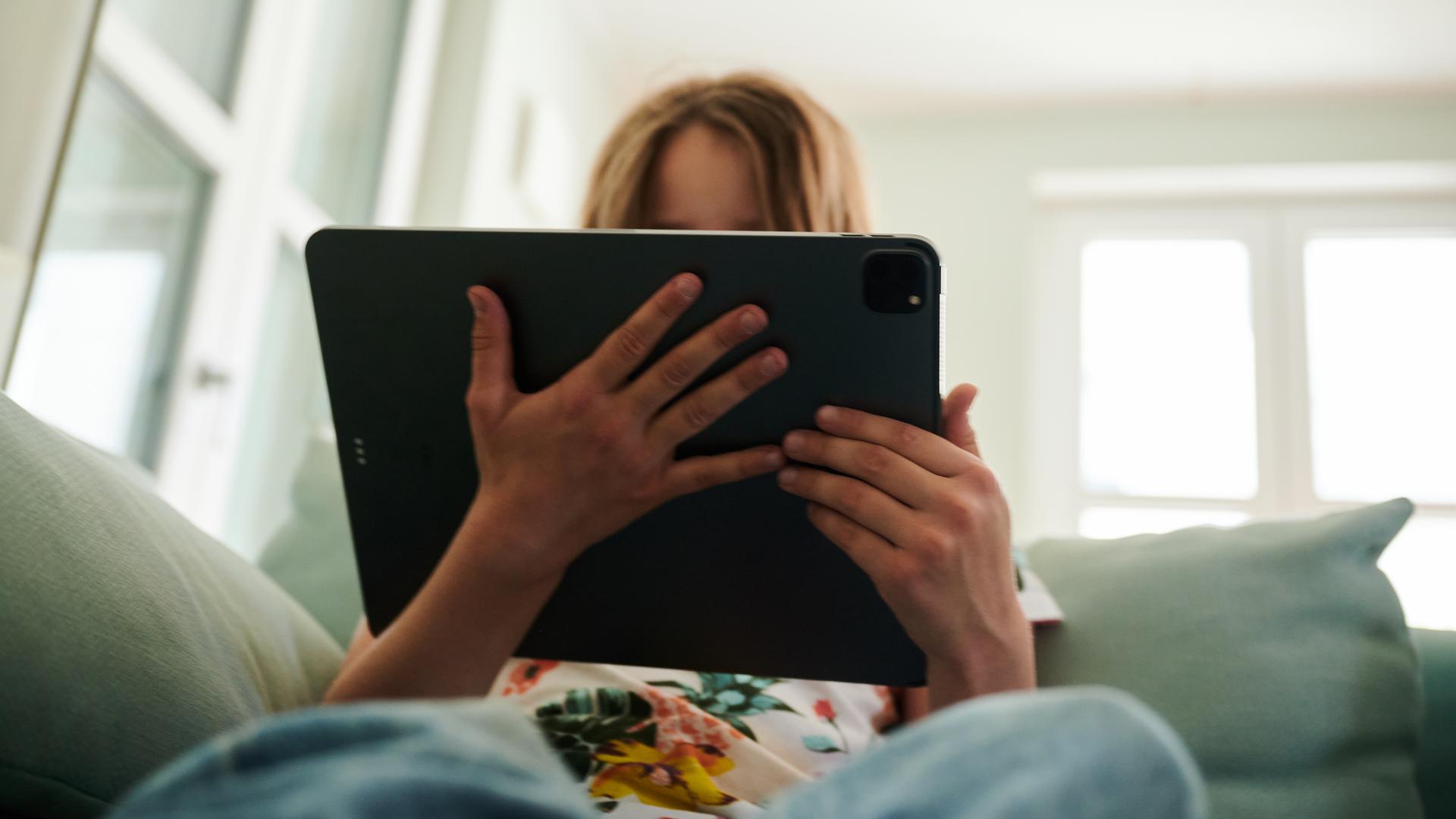 Mädchen sitzt mit Tablet auf dem Sofa