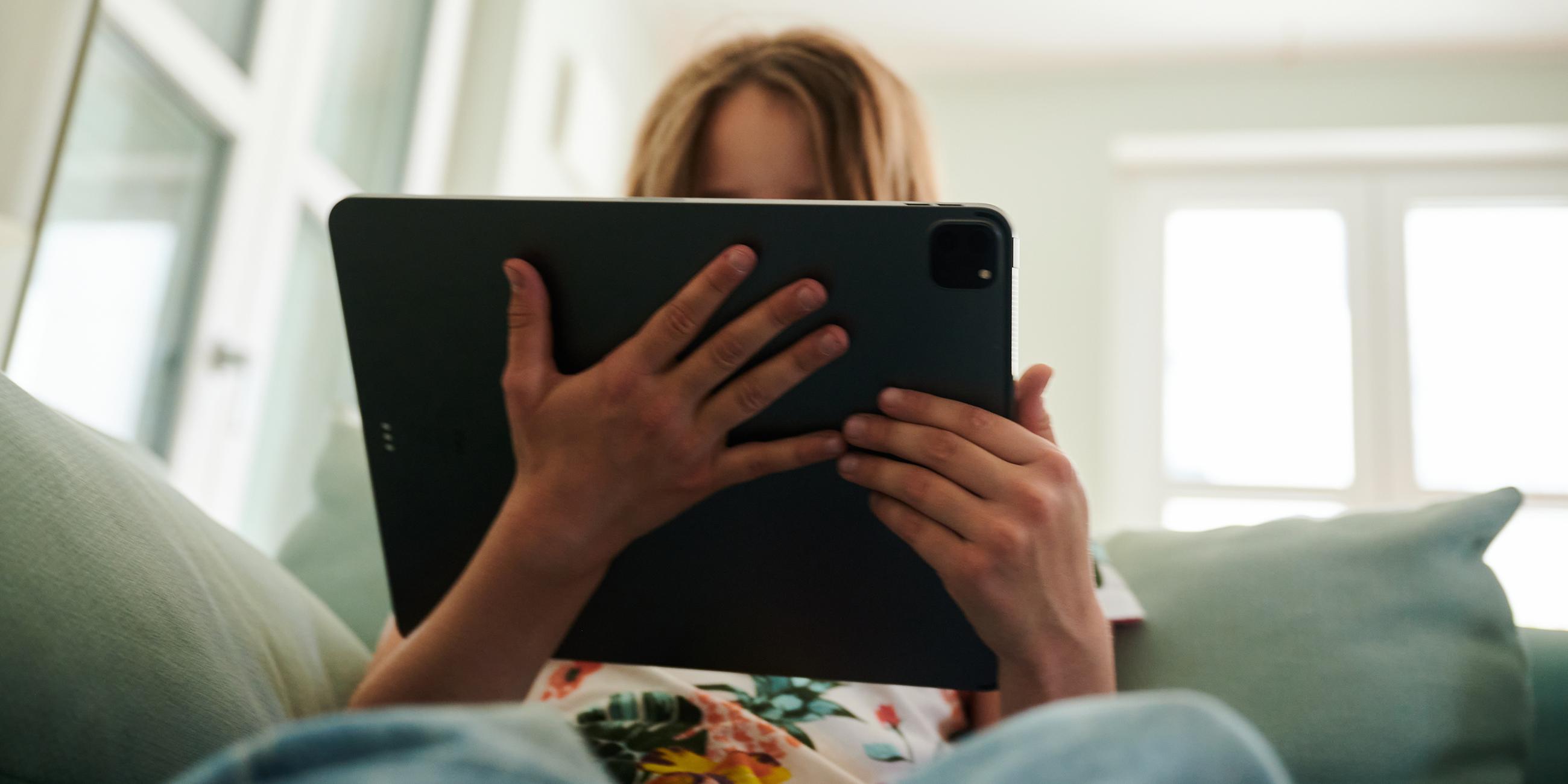 Mädchen sitzt mit Tablet auf dem Sofa