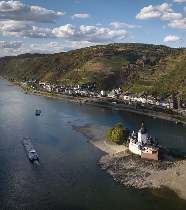 06.08.2026, Rheinland-Pfalz, Kaub: Ein Schiff fährt auf dem Rhein bei einem niedrigen Wasserstand an der Burg Pfalzgrafenstein vorbei. (Aufnahme mit Drohne)