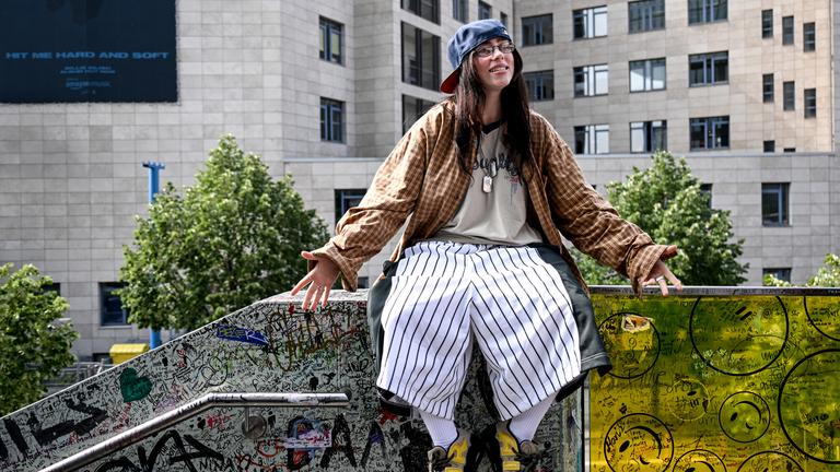 Die US-amerikanische Sängerin Billie Eilish sitzt auf einem Mauervorsprung eines Treppengeländers in Berlin, das als die "Billie Eilish-Wand" bekannt ist.