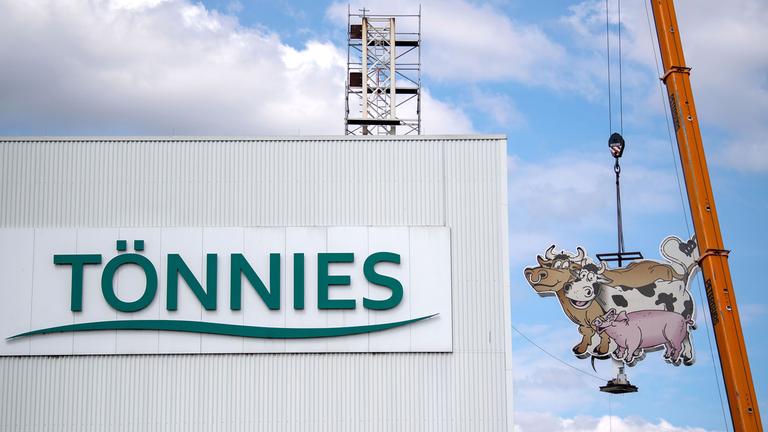 Das alte Logo von dem Fleischverarbeiter und Schlachtkonzern Tönnies schwebt an einem Schwerlastkran in der Luft.