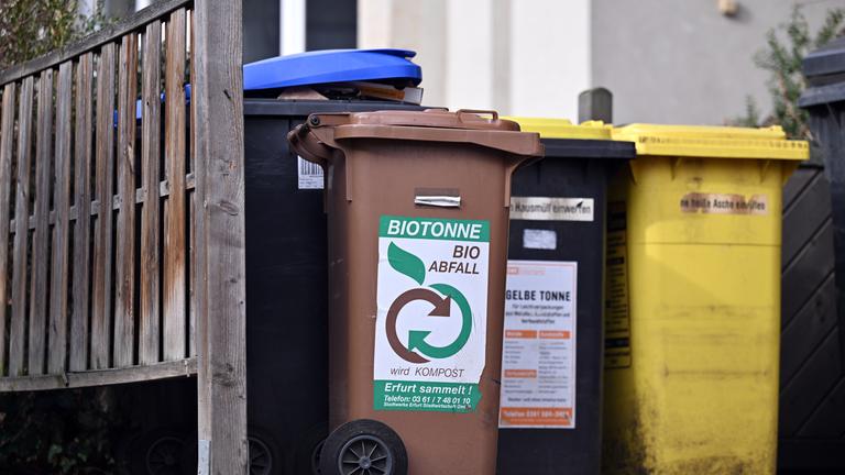 Eine Biotonne steht mit Tonnen für Wertstoffe, Papier und Restmüll vor einem Wohnhaus nebeneinander.