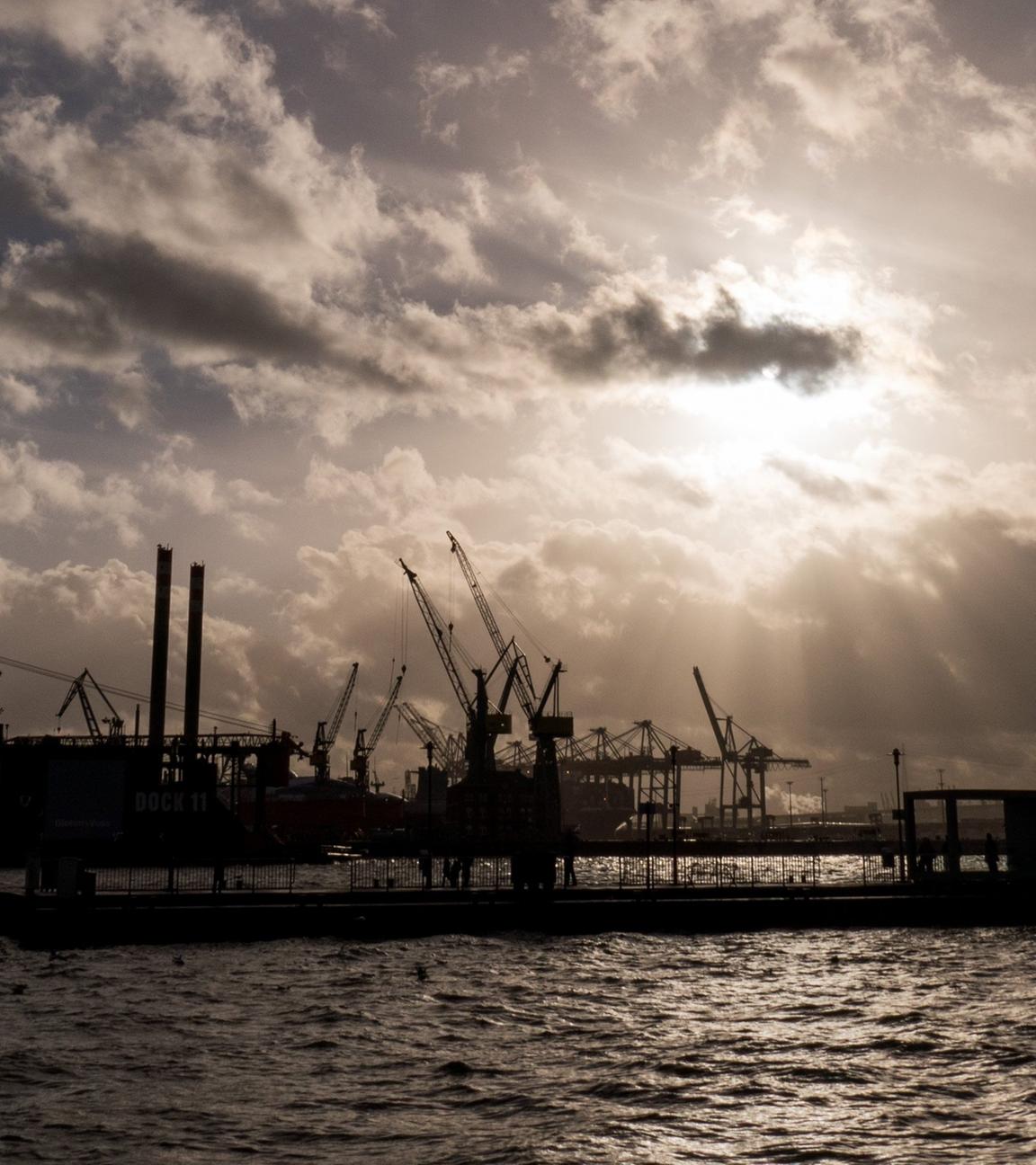 Symbolbild: Durch dunkle Regenwolken scheint etwas Sonne über den Hafenanlagen in Hamburg