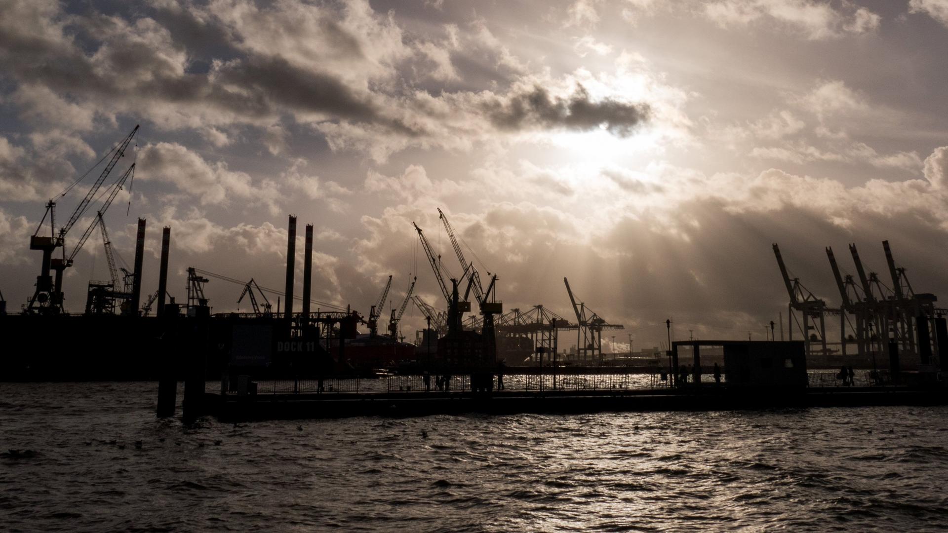 Symbolbild: Durch dunkle Regenwolken scheint etwas Sonne über den Hafenanlagen in Hamburg