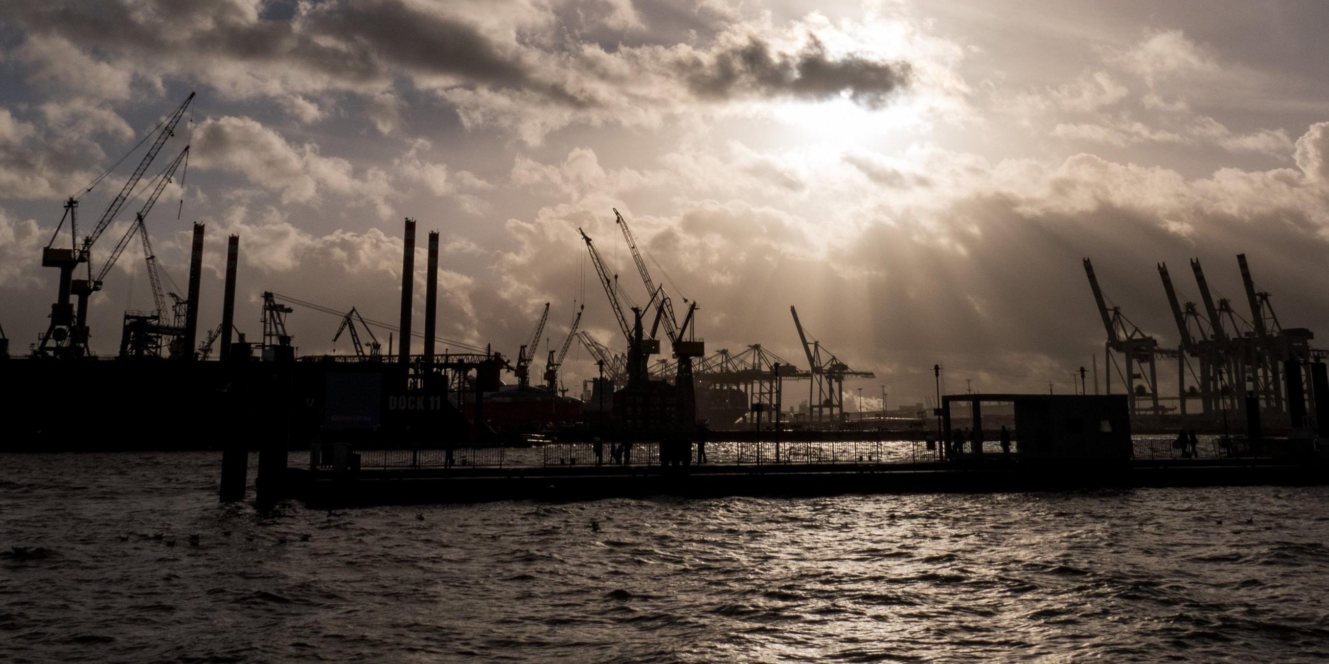Symbolbild: Durch dunkle Regenwolken scheint etwas Sonne über den Hafenanlagen in Hamburg