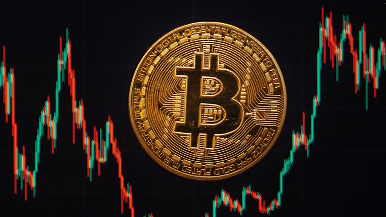 Symbolbild: Eine Bitcoin-Münze liegt auf einem Bildschirm, der den Bitcoin - US-Dollar Kurs zeigt. 