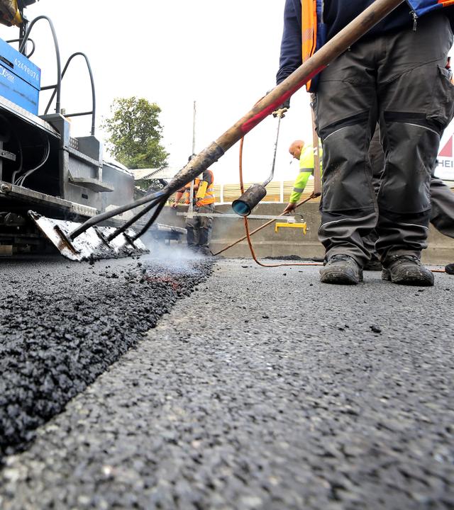 02.10.2020, Nordrhein-Westfalen, Mülheim: Arbeiter tragen auf einer Autobahn eine neue Asphaltdecke auf.