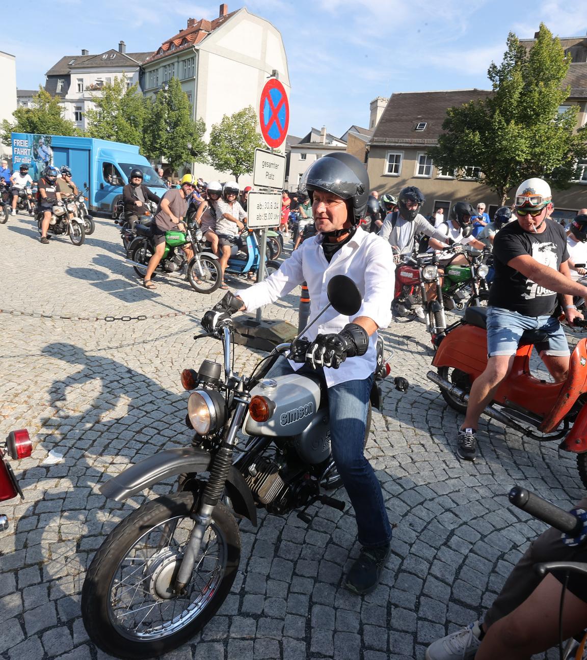 Ein amnn mit Motorradhelm sitzt auf einem Moped.