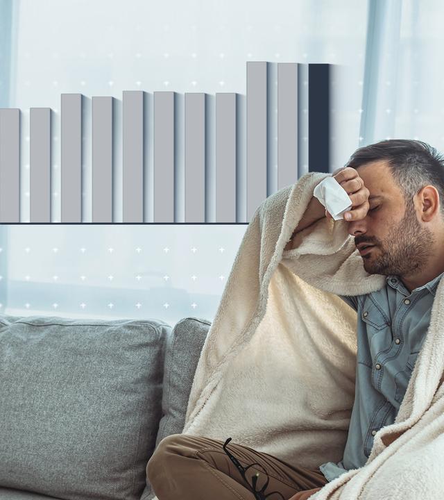 Ein kranker Mann sitzt auf einem Sofa, ist in eine Decke eingewickelt und hält sich den Kopf, als hätte er Kopfschmerzen. In seiner Hand hält er ein Taschentuch. Neben seinem Kopf ist eine Grafik abgebildet.