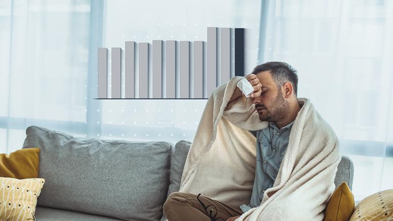 Ein kranker Mann sitzt auf einem Sofa, ist in eine Decke eingewickelt und hält sich den Kopf, als hätte er Kopfschmerzen. In seiner Hand hält er ein Taschentuch. Neben seinem Kopf ist eine Grafik abgebildet.