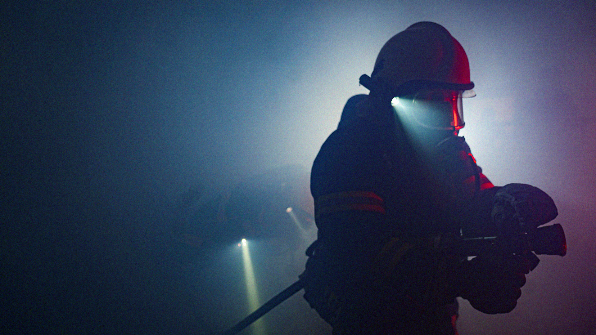 Stromtechniker mit Schutzhelm rollt in Dunkelheit und Nebel Kabeltrommel auf