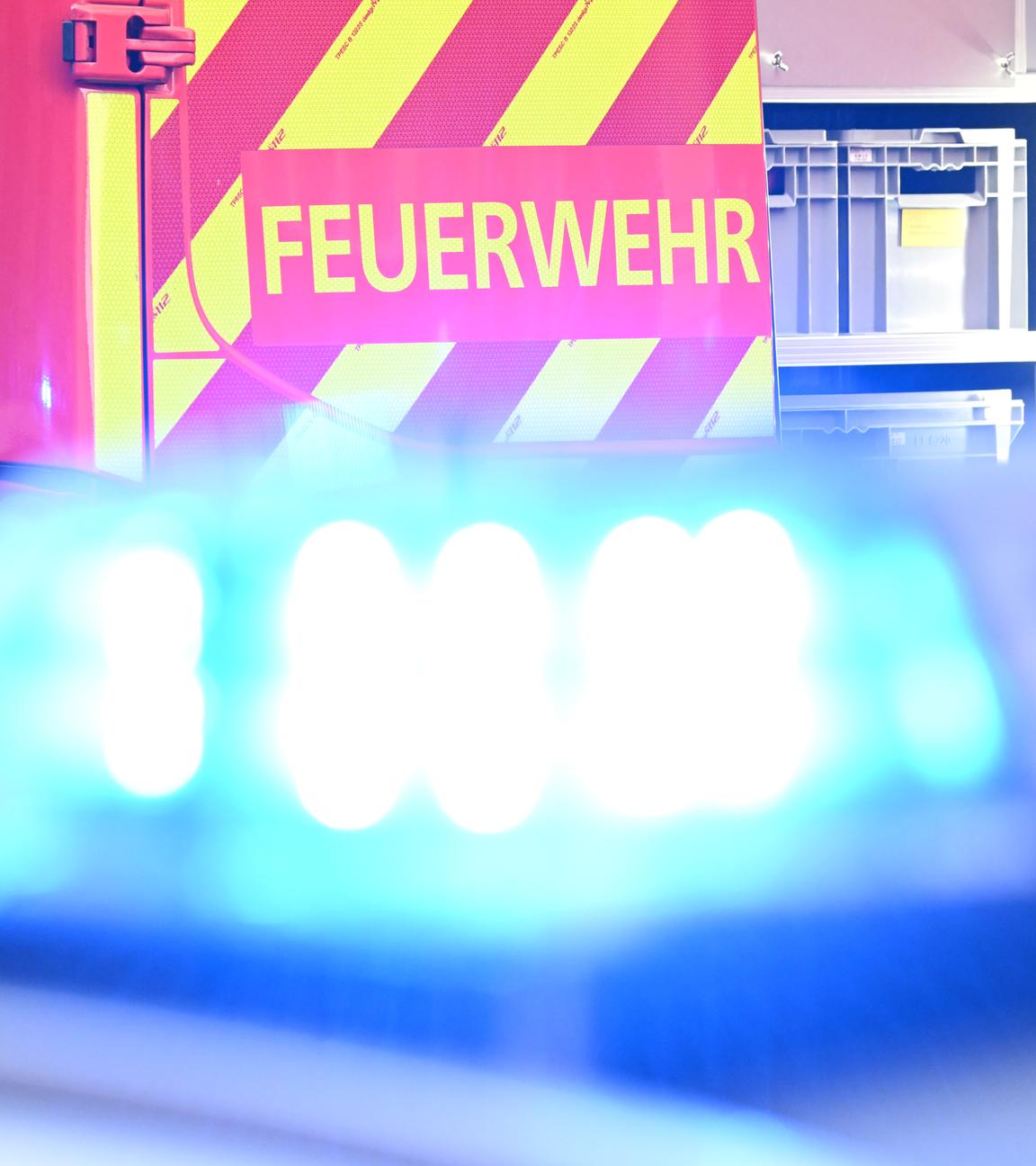 Blaulicht im Vordergrund, dahinter ein Feuerwehr-Fahrzeug mit der Aufschrift "Feuerwehr".
