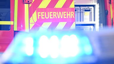 Ein Fahrzeug der Feuerwehr steht bei einem Einsatz auf einer Straße, während im Vordergrund das Blaulicht eines Polizeifahrzeugs zu sehen ist. (Archiv)
