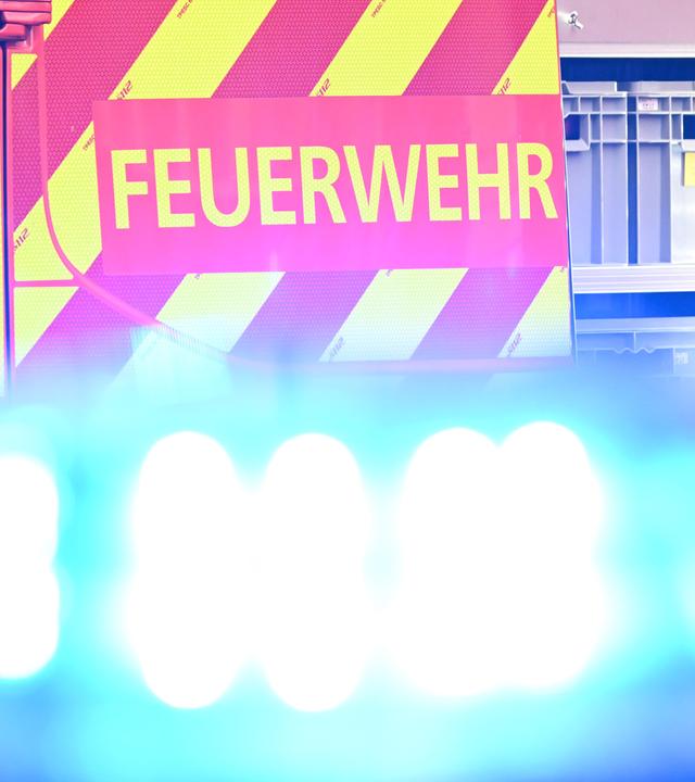  Ein Fahrzeug der Feuerwehr steht bei einem Einsatz auf einer Straße, während im Vordergrund das Blaulicht eines Polizeifahrzeugs zu sehen ist. (Archiv)