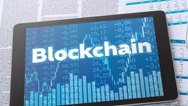 Tablet mit Schrift "Blockchain" auf Finanzdokumenten neben Taschenrechner