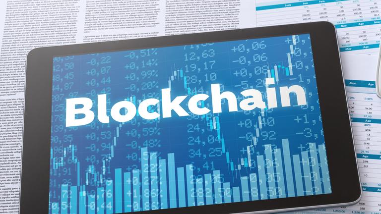 Tablet mit Schrift "Blockchain" auf Finanzdokumenten neben Taschenrechner