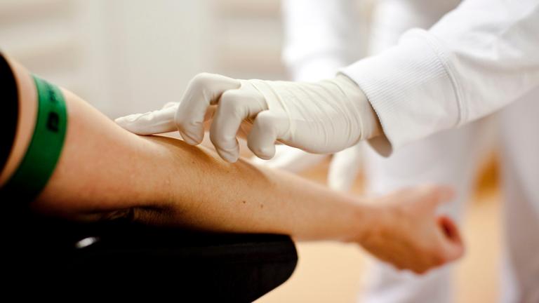 Einem Patienten wird in einer Praxis Blut von Arztpersonal abgenommen.