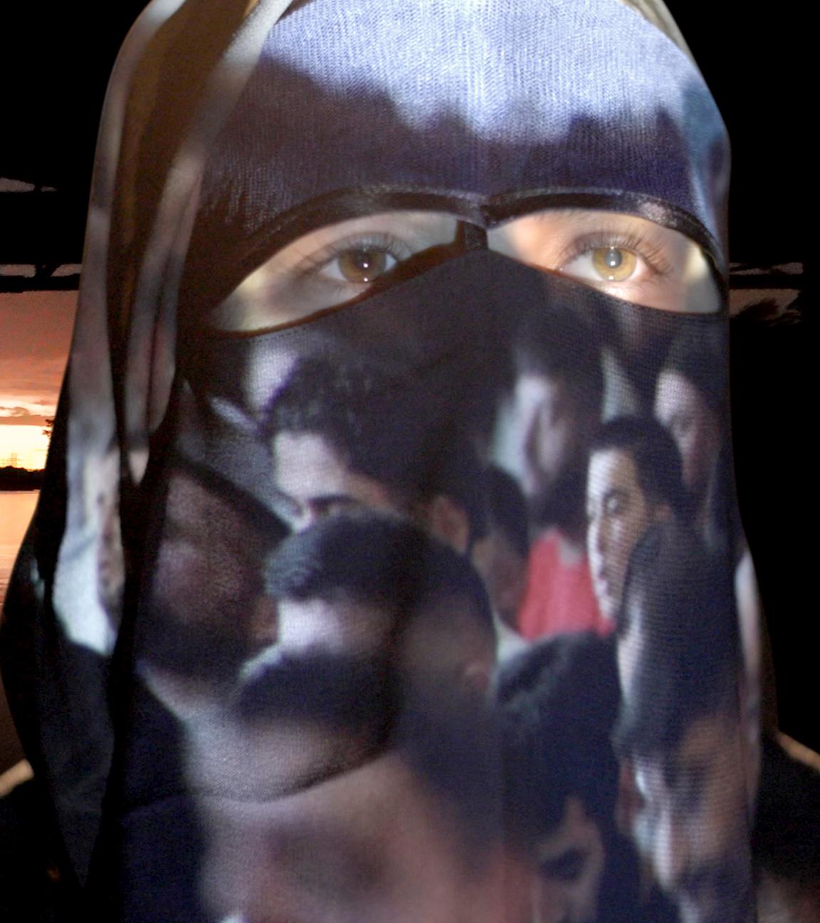 Eine Frau mit Burka, auf der Bilder projiziert werden, vor einer Flusslandschaft 