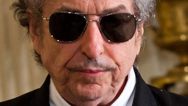 Bob Dylan mit Anzug, schwarzer Sonnenbrille und Fliege. 
