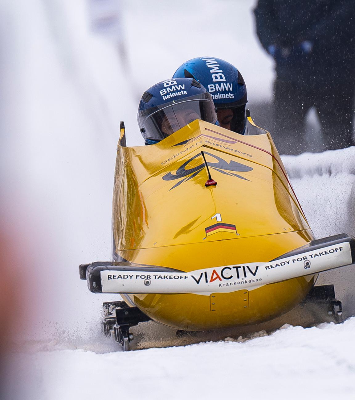 zwei Personen in einem gelben Sportbob sitzend auf einer Bobbahn