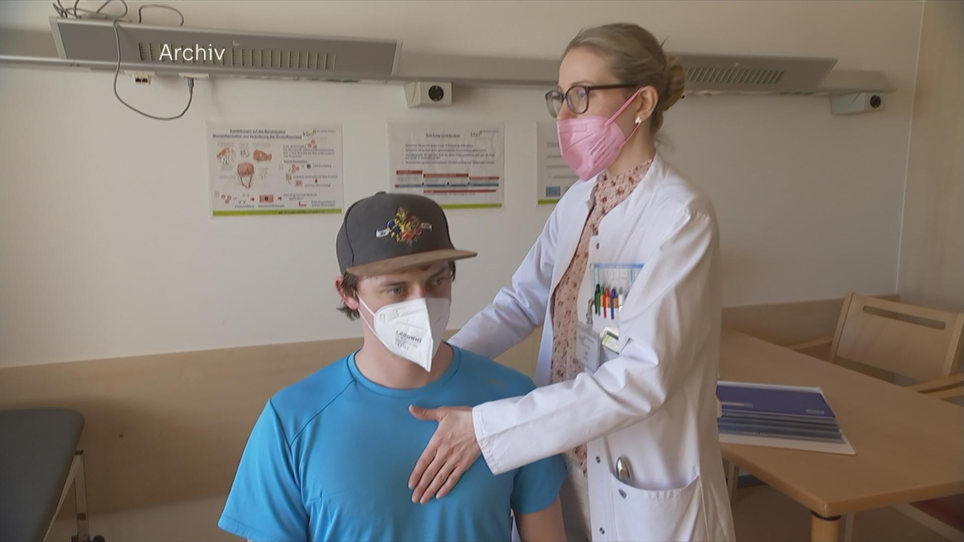 Eine Ärztin tastet einen sitzenden Patienten an der Brust ab