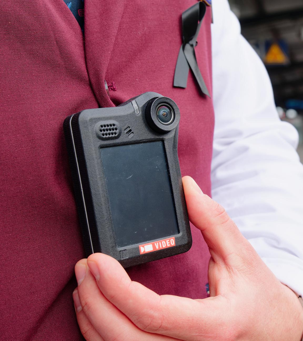  Ein Kundenbetreuer steht bei einem Pressetermin der Deutsche Bahn (DB) auf einem Bahnsteig neben einem Regionalzug und trägt eine Bodycam an der Dienstkleidung