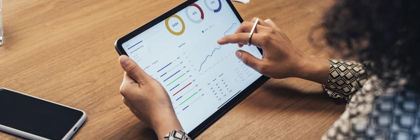 Man sieht eine Frau von hinten, die sich auf einem Tablet Aktienkurse anschaut.