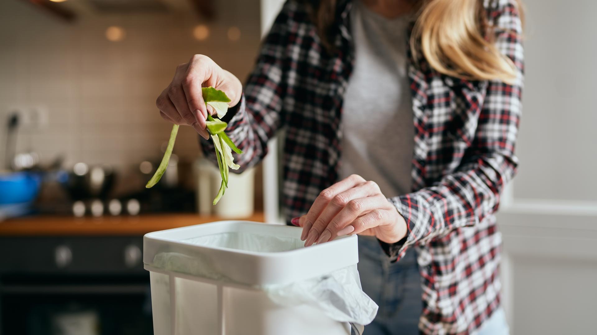 Eine Frau gibt Gurkenschalen in einen Eimer, der in einer Küche steht.