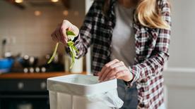 A woman puts cucumber peels in a bucket in the kitchen.