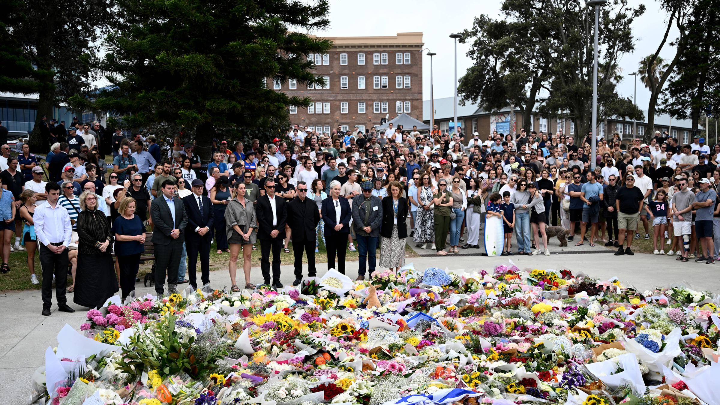 Eine Menschenmenge steht trauernd vor niedergelegten Blumen am 15.12.2025 am Bondi Beach in Australien.