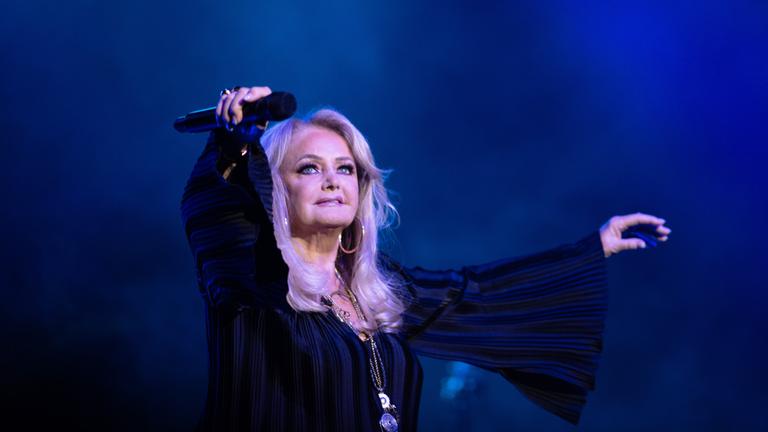 Bonnie Tyler ist während einer Musik-Performance zu sehen, sie hält ein Mikro in der Hand.