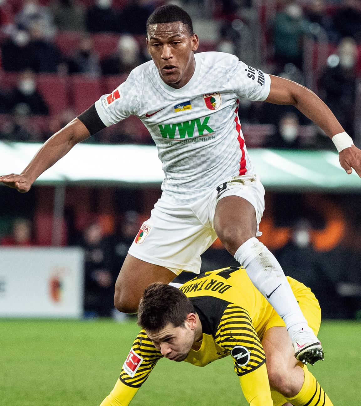 27.02.2022, Bayern, Augsburg: Fußball: Bundesliga, FC Augsburg - Borussia Dortmund, 24. Spieltag, WWK-Arena. Carlos Gruezo von Augsburg (oben) und Raphael Guerreiro von Borussia Dortmund im Zweikampf um den Ball.