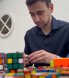 Ein Mann sitzt an einem Tisch mit vielen Rubik Cubes