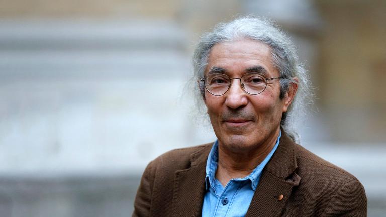 Porträtfoto eines Mannes mit zurückgebundenen grauen Haaren und runder Metallbrille, der in die Kamera lächelt.