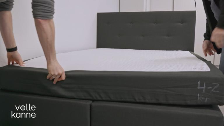 Personen stehen neben Boxspringbett