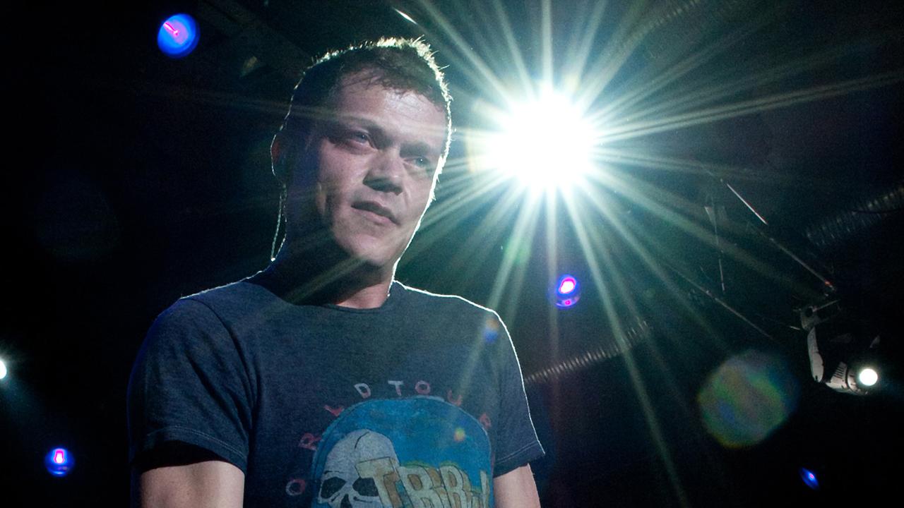 Der Sänger Brad Arnold steht auf der Bühne, von hinten strahlt Scheinwerferlicht in die Kamera.