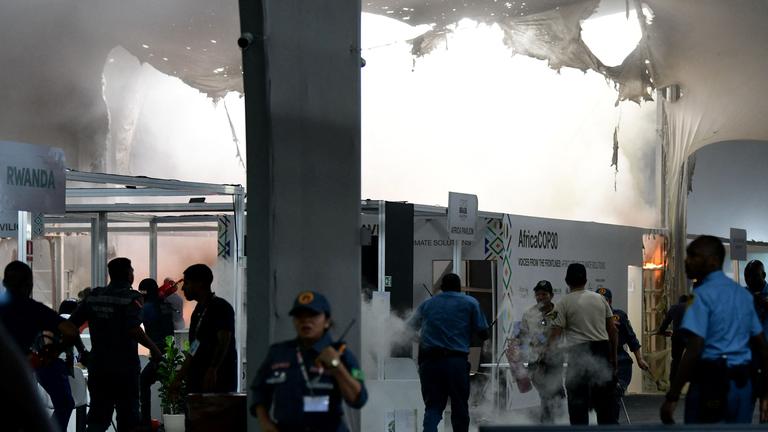 Rauch steigt nach einem Brand auf der Weltklimakonferenz empor. Viele Menschen stehen um den Ort des Geschehens.