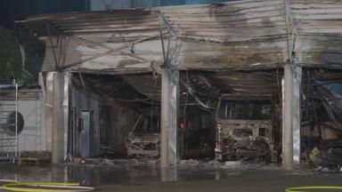 Blick auf die stark beschädigte Fahrzeughalle eines Feuerwehrhauses in Offenbach. Mehrere ausgebrannte Einsatzfahrzeuge sind zu sehen. Trümmer liegen vor der Halle; der Boden ist nass.