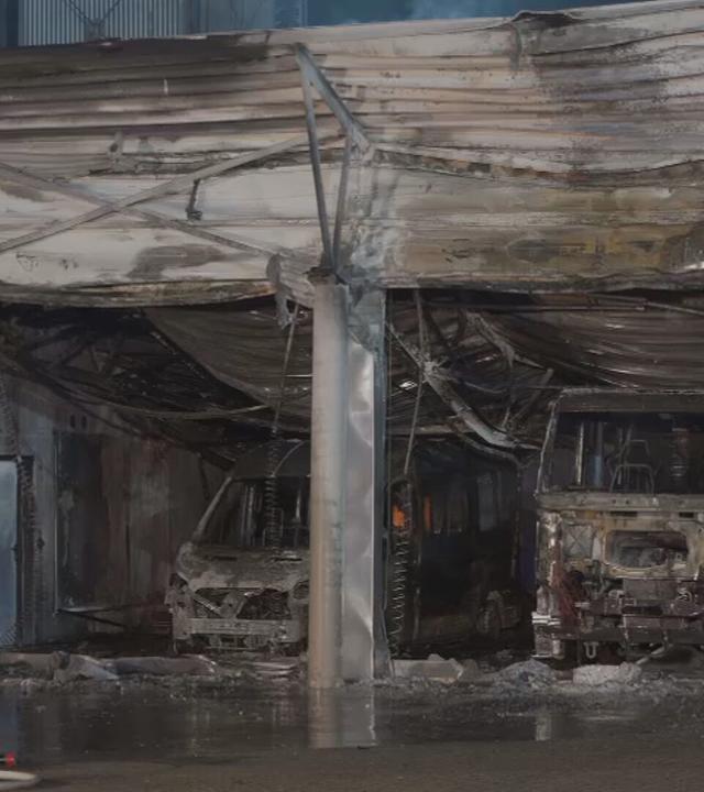 Blick auf die stark beschädigte Fahrzeughalle eines Feuerwehrhauses in Offenbach. Mehrere ausgebrannte Einsatzfahrzeuge sind zu sehen. Trümmer liegen vor der Halle; der Boden ist nass.