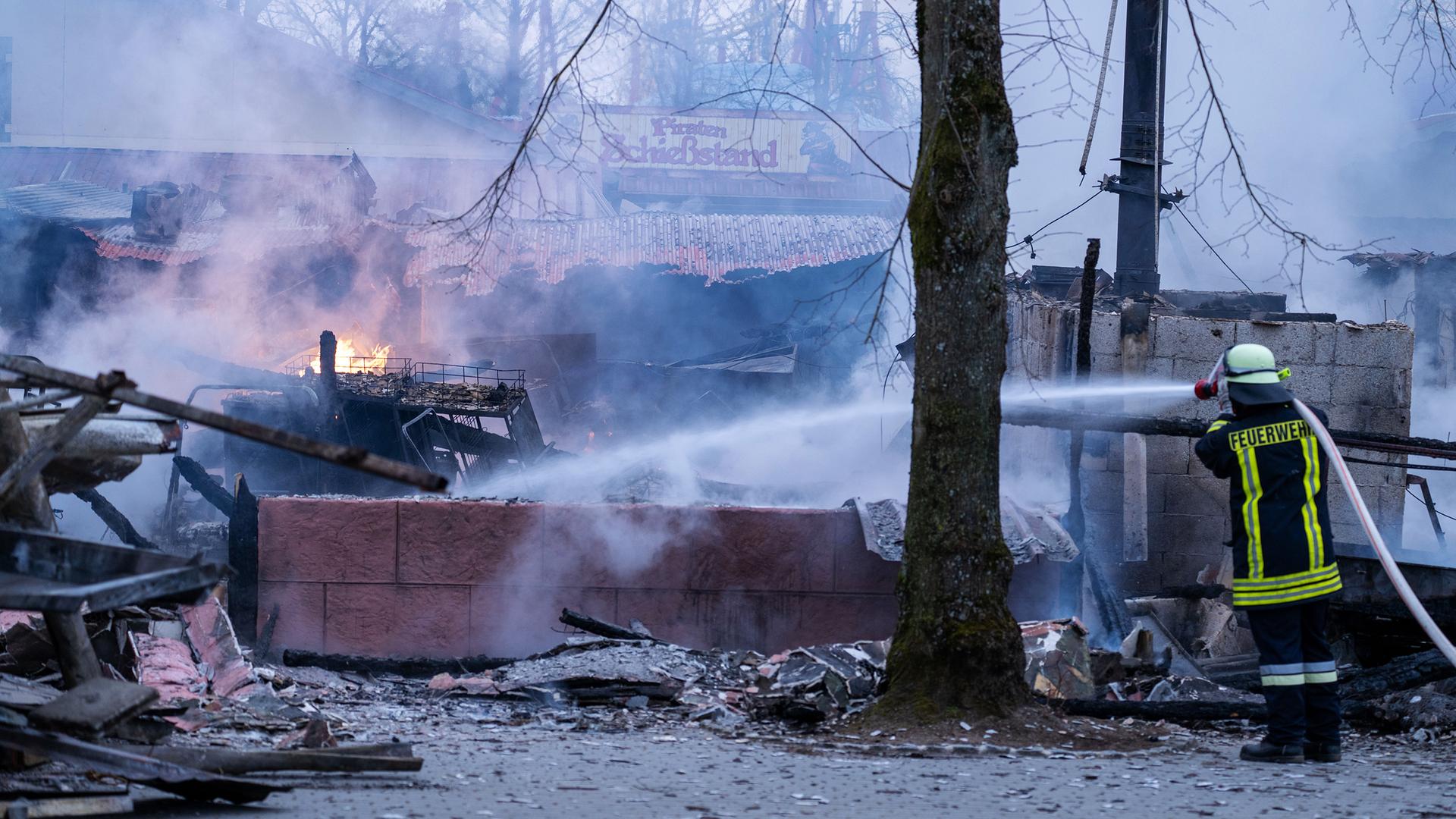 Ein Feuerwehrmann strahlt Wasser auf verkohlte Gebäude- und Einrichtungsteile, im Hintergrund ist der Schrifzug "Piraten Schießstand" zu lesen, aufgenommen am 17.03.2025