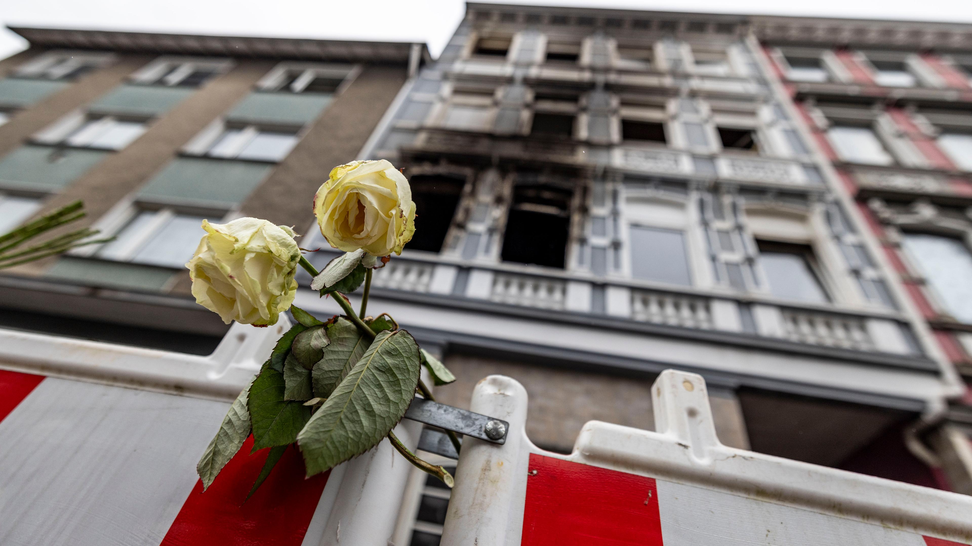 Eine weiße Rose hängt an einer Absperrbake vor dem Brandort in Solingen. Im Prozess um den Tod einer vierköpfigen Familie in Solingen geht es vor Gericht weiter um das Motiv des mutmaßlichen Täters.