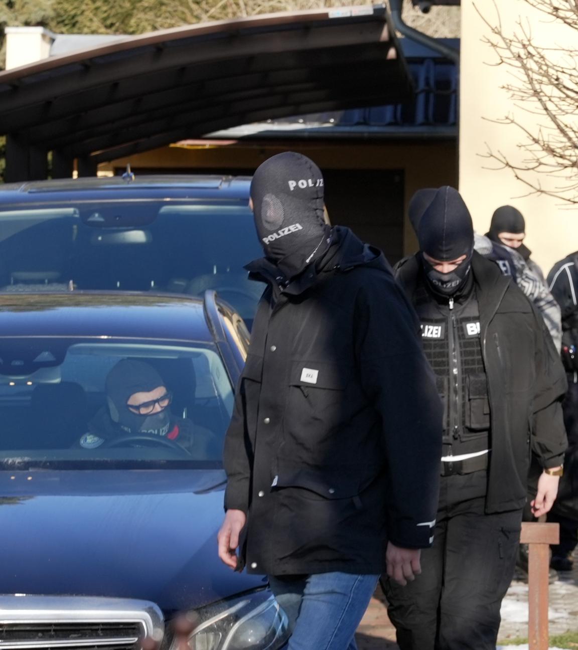 Vermummte Einsatzkräfte des Bundeskriminalamtes (BKA) gehen nach einer Durchsuchung vor einem Haus entlang.