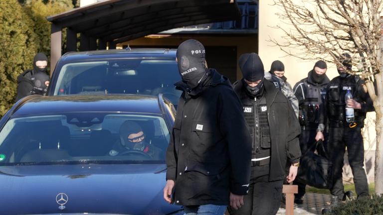 Vermummte Einsatzkräfte des Bundeskriminalamtes (BKA) gehen nach einer Durchsuchung vor einem Haus entlang.