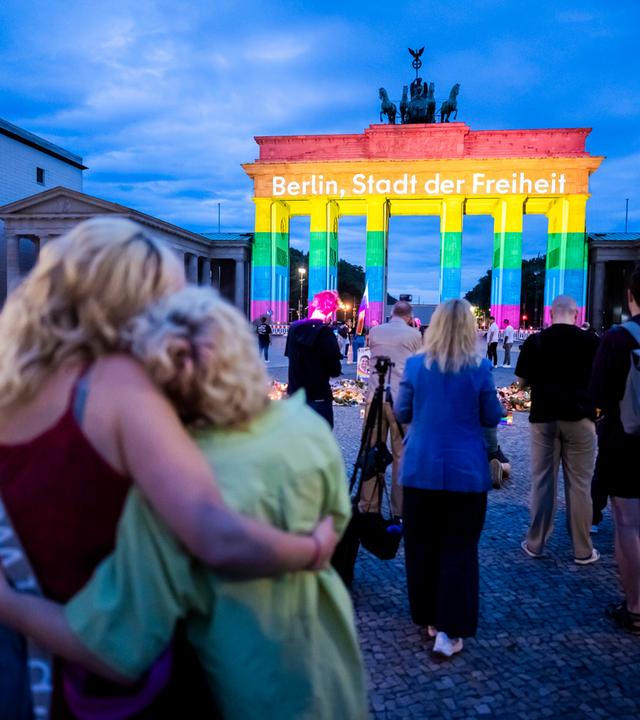 Menschen vor dem Brandenburger Tor, dass in Regenbogenfarben leuchtet. Darauf ist der Schriftzug zu lesen: "Berlin, Stadt der Freiheit"