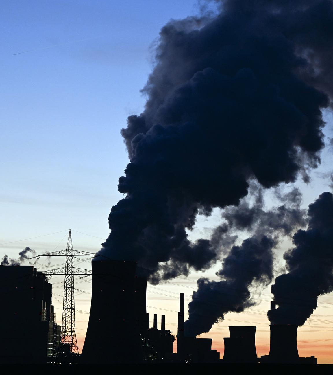 Hinter dem Braunkohlekraftwerk Neurath ist die Sonne untergegangen und Rauch und Dampf steigen in den Abendhimmel