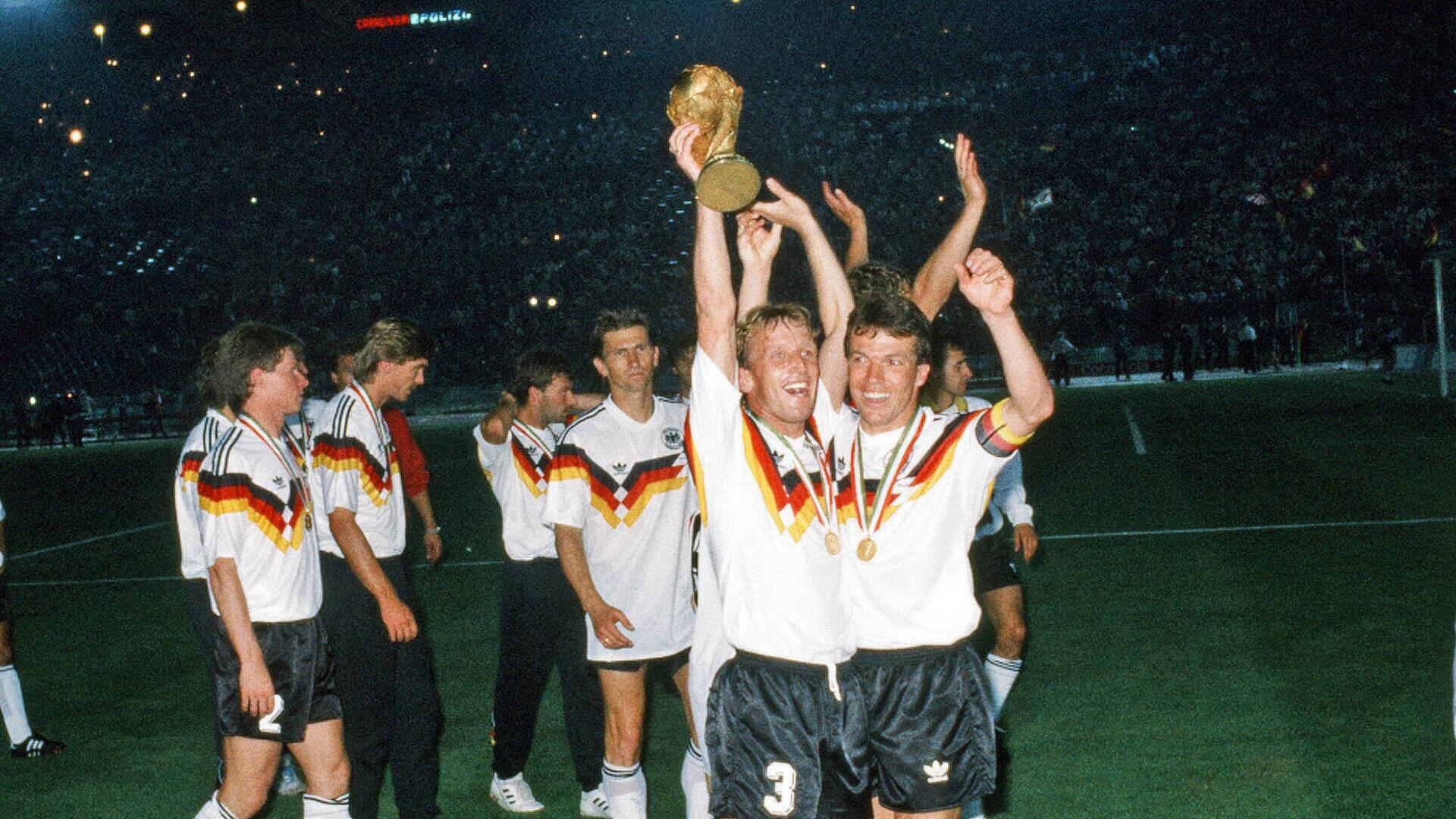 zwei Fußballer (Andreas Brehme sowie Lothar Matthäus) strecken den Weltmeisterpokal in die Höhe 