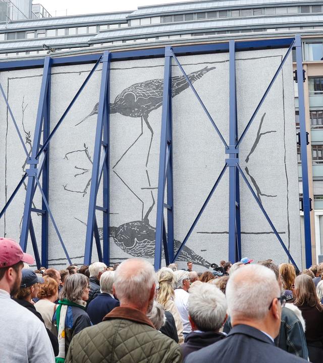 Auf dem Bild ist ein 12 Meter hohes Mosaik zu sehen, das an die Opfer der Terroranschläge in Norwegen am 22. Juli 2011 erinnern soll. Auf dem Bild sind außerdem Menschen zu sehen, die vor dem Moasik stehen und es betrachten.